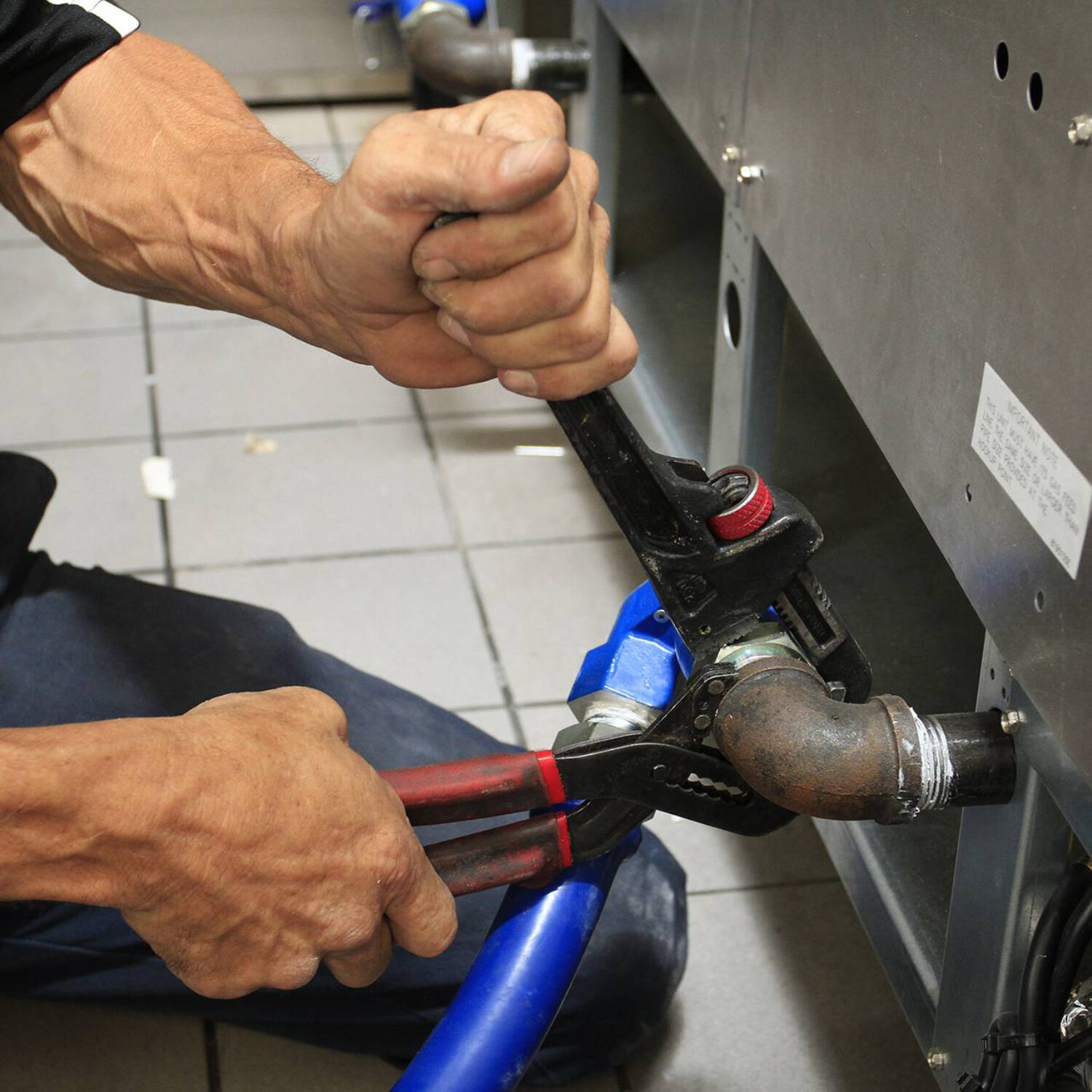 A CES Factory Certified Installer Installing a Commercial Gas Hose on a FryMaster Fryer during a Commercial Kitchen Installation